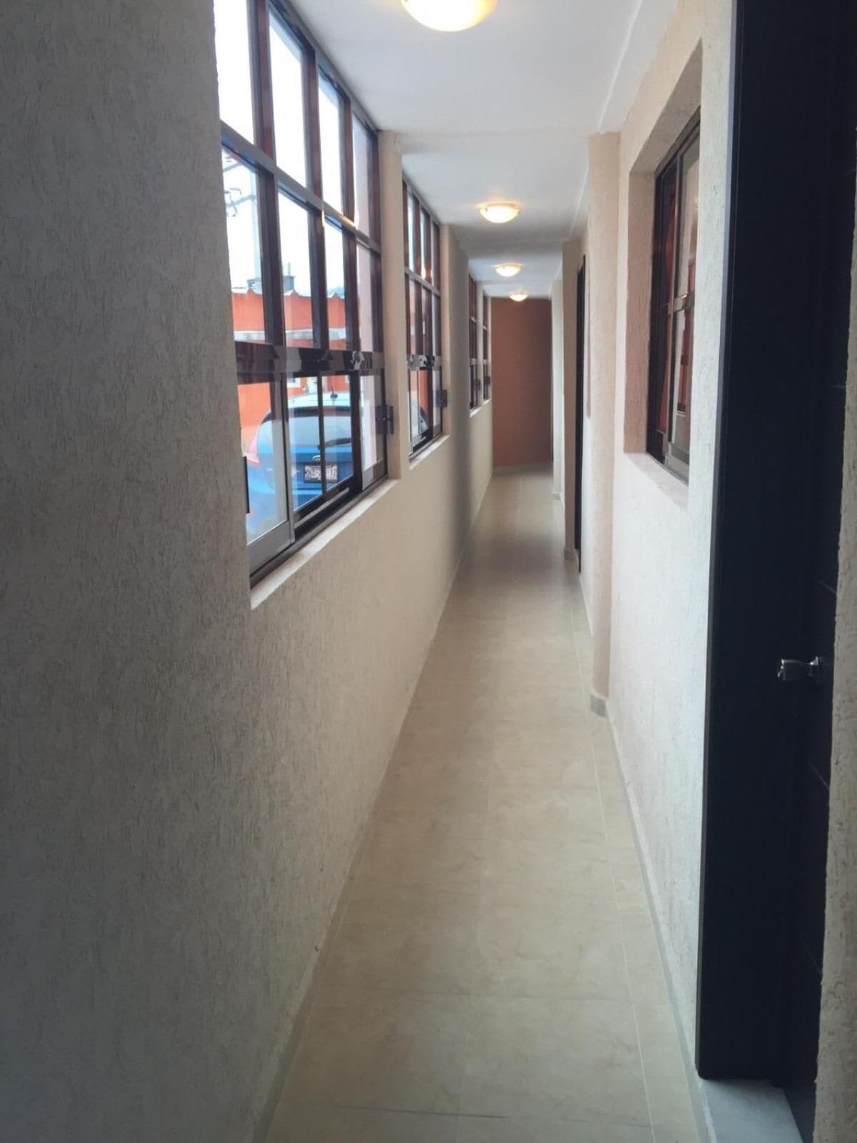 A corridor with large windows, a tiled floor, and a door on the right.