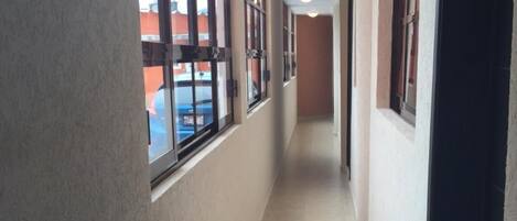 A corridor with large windows, a tiled floor, and a door on the right.