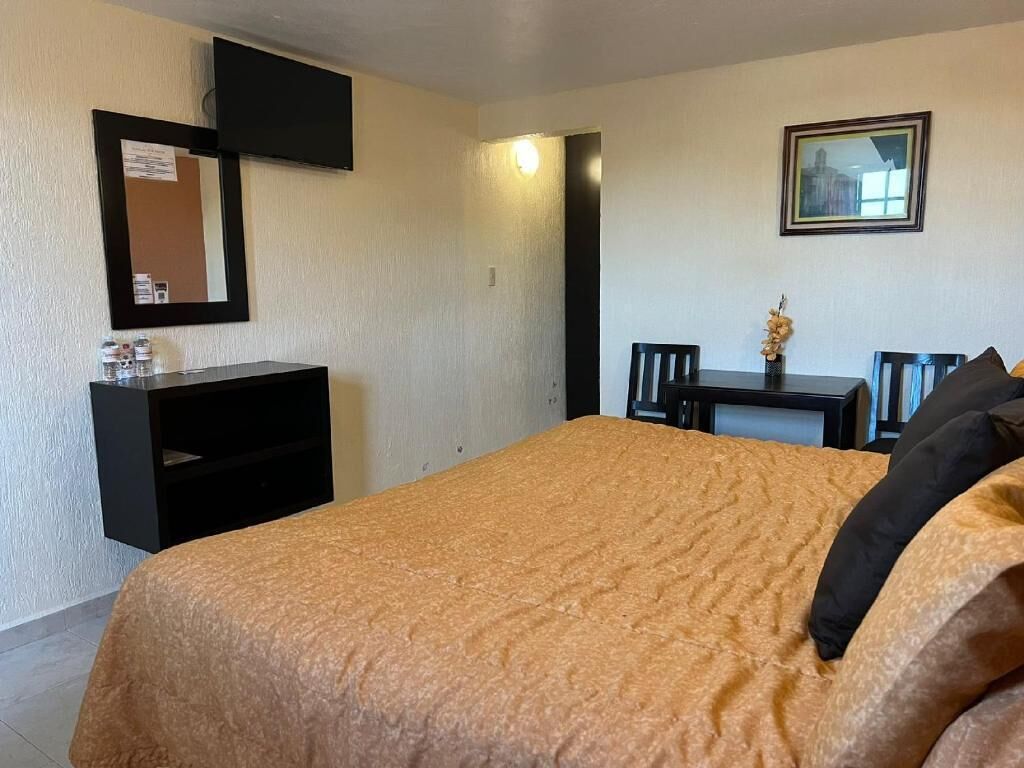 Ein Hotelzimmer mit Bett, Schreibtisch, Sessel, an der Wand montiertem Fernseher und einem gerahmten Bild.
