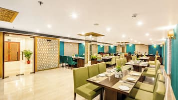 A spacious restaurant with multiple dining areas, green upholstered seating, and a modern interior design.