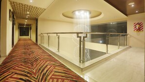 A hotel corridor with a patterned carpet, a glass railing, and a chandelier.