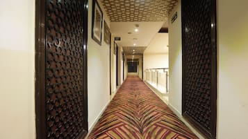 A hotel corridor with patterned carpet, wooden doors, and a lift sign.