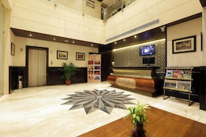 A hotel lobby with a reception desk, a large digital display, a patterned floor, and a potted plant. - Vesta Sapphire Jaipur - A City Center Hotel (Jaipur)