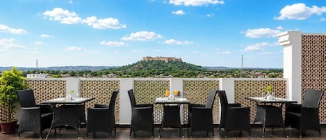 An outdoor patio with tables and chairs, a view of a hill with a castle, and a clear sky.