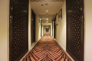 A hotel hallway with patterned carpet, wooden doors, and a ceiling with a geometric design.