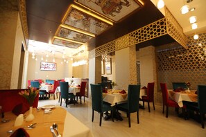 A restaurant with multiple tables and chairs, some with red cushions. - Vesta Sapphire Jaipur - A City Center Hotel (Jaipur)