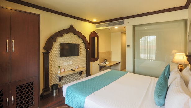 A hotel room with a large bed, a wooden wardrobe, a small table with a kettle, and a mirror on the wall.