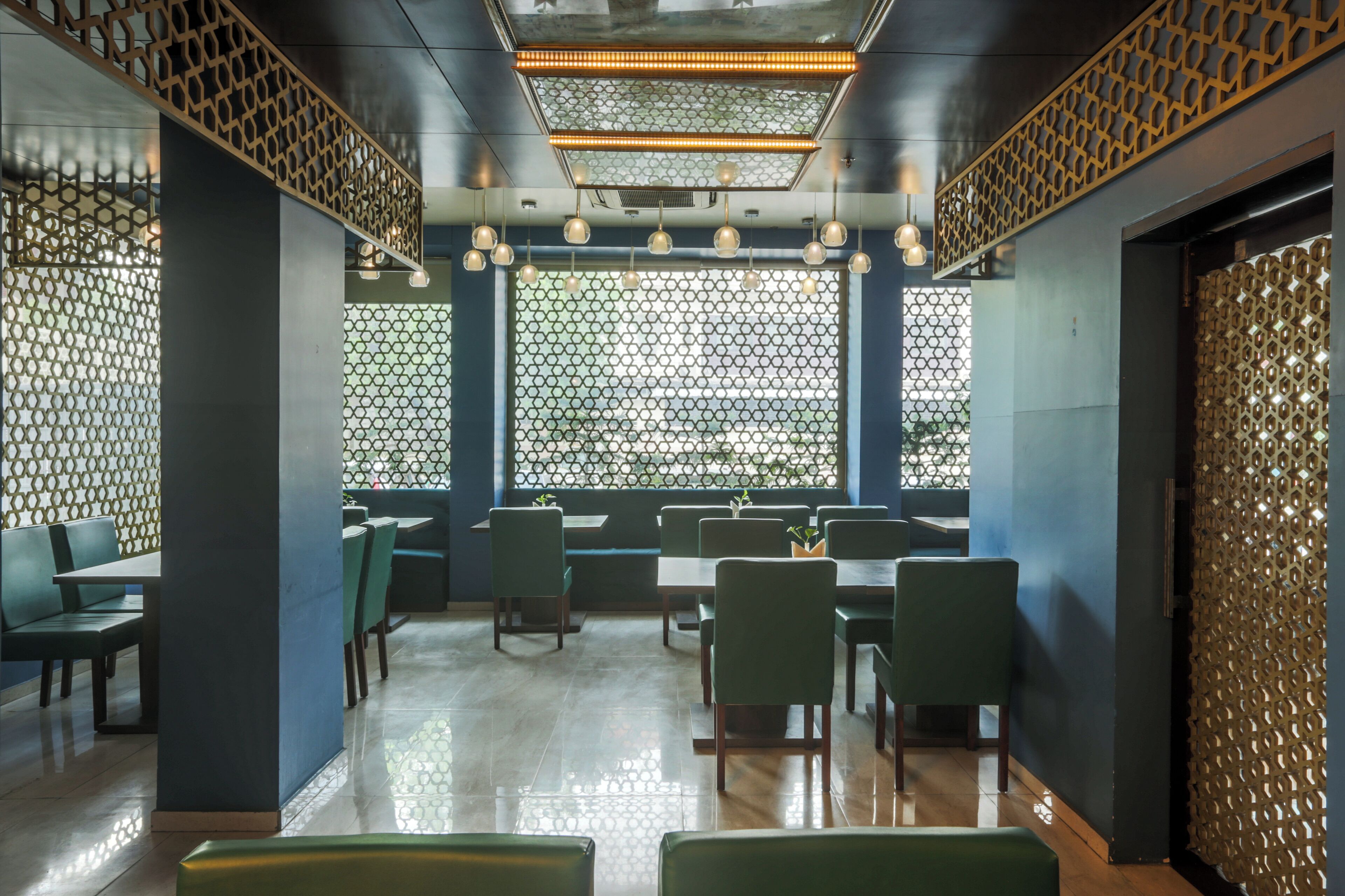 Interior de restaurante con diseño moderno, destacando una pared con diseño, asientos verdes e iluminación colgante.
