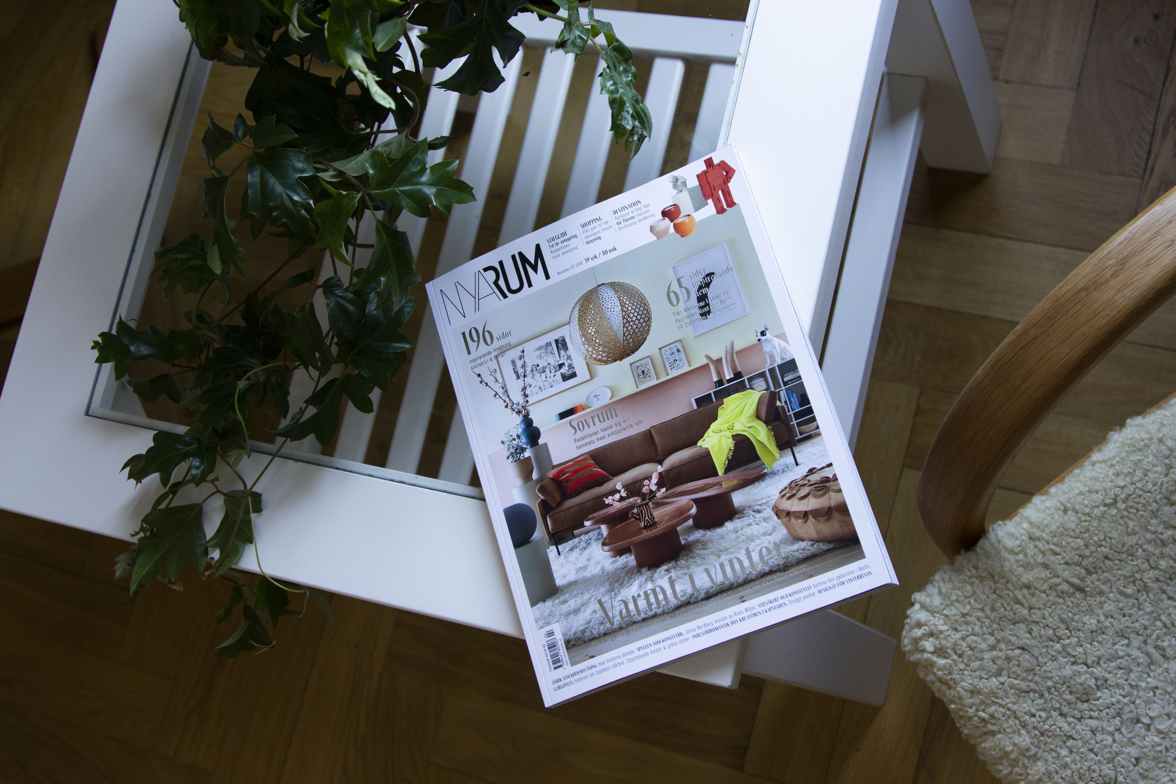 A magazine on a white table with a plant beside it.