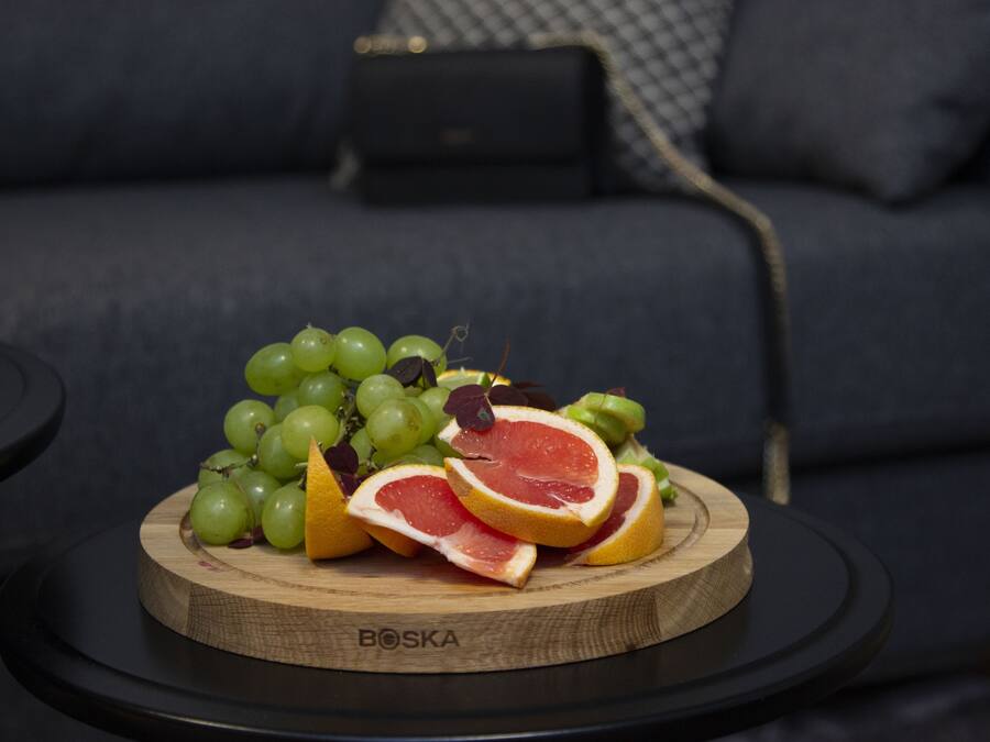 Une planche en bois sur laquelle on a disposé des raisins verts et des demi-pamplemousses, le tout posé sur une table ronde noire. Un canapé sombre se trouve à l’arrière-plan.