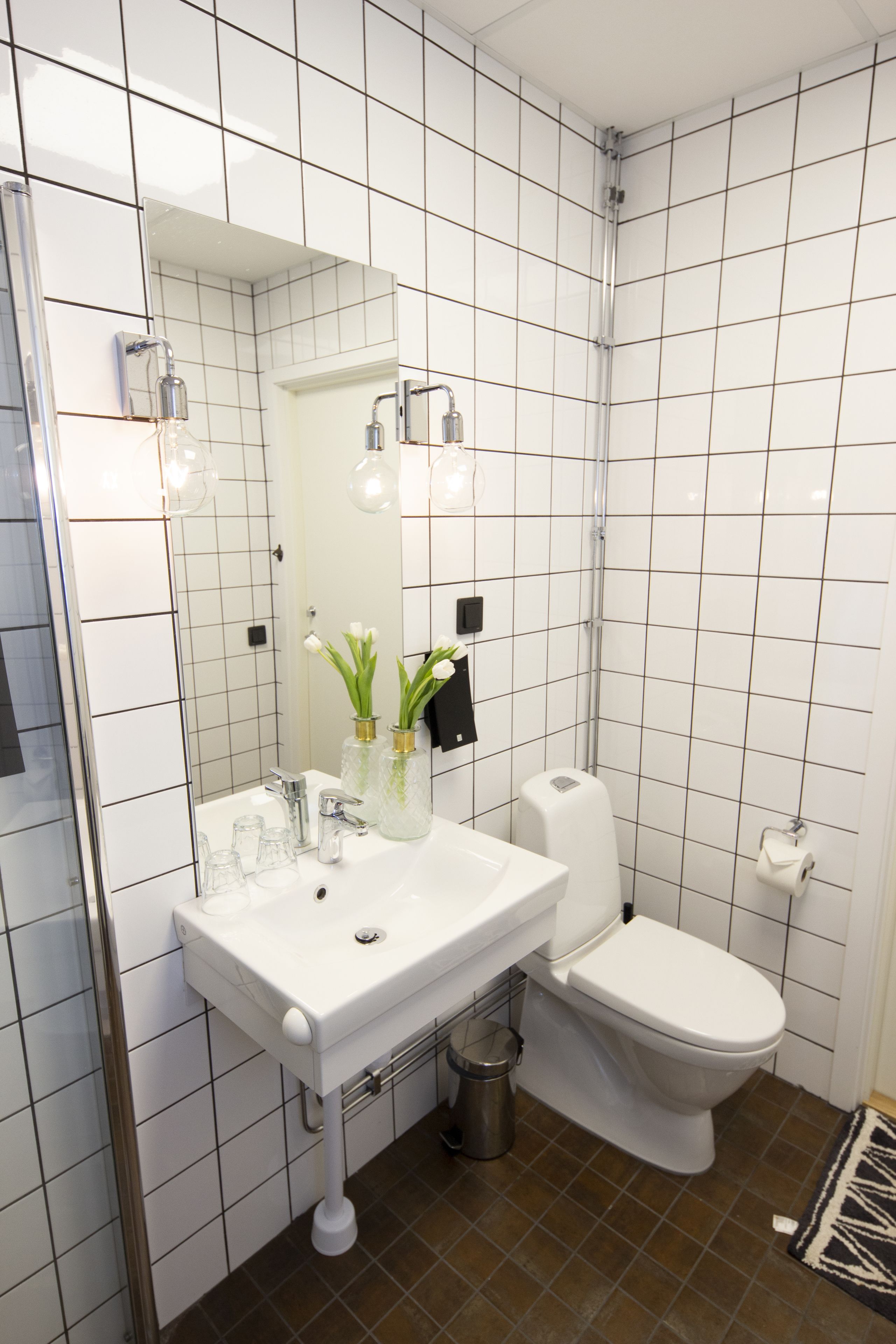 A bathroom with a white sink, mirror, and toilet. There are two glass jars with flowers on the sink.