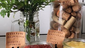Una mesa con un tarro de vidrio con líquido rosa, un tarro de vidrio con líquido amarillo, un florero de vidrio con flores rosas y un tarro de tapones de corcho.