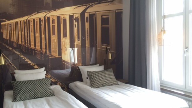 A hotel room with two beds, a large window, and a mural of a train. - Livin Station (Örebro)