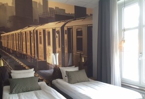 Habitación de hotel con dos camas, un ventanal grande y un mural de un tren.
