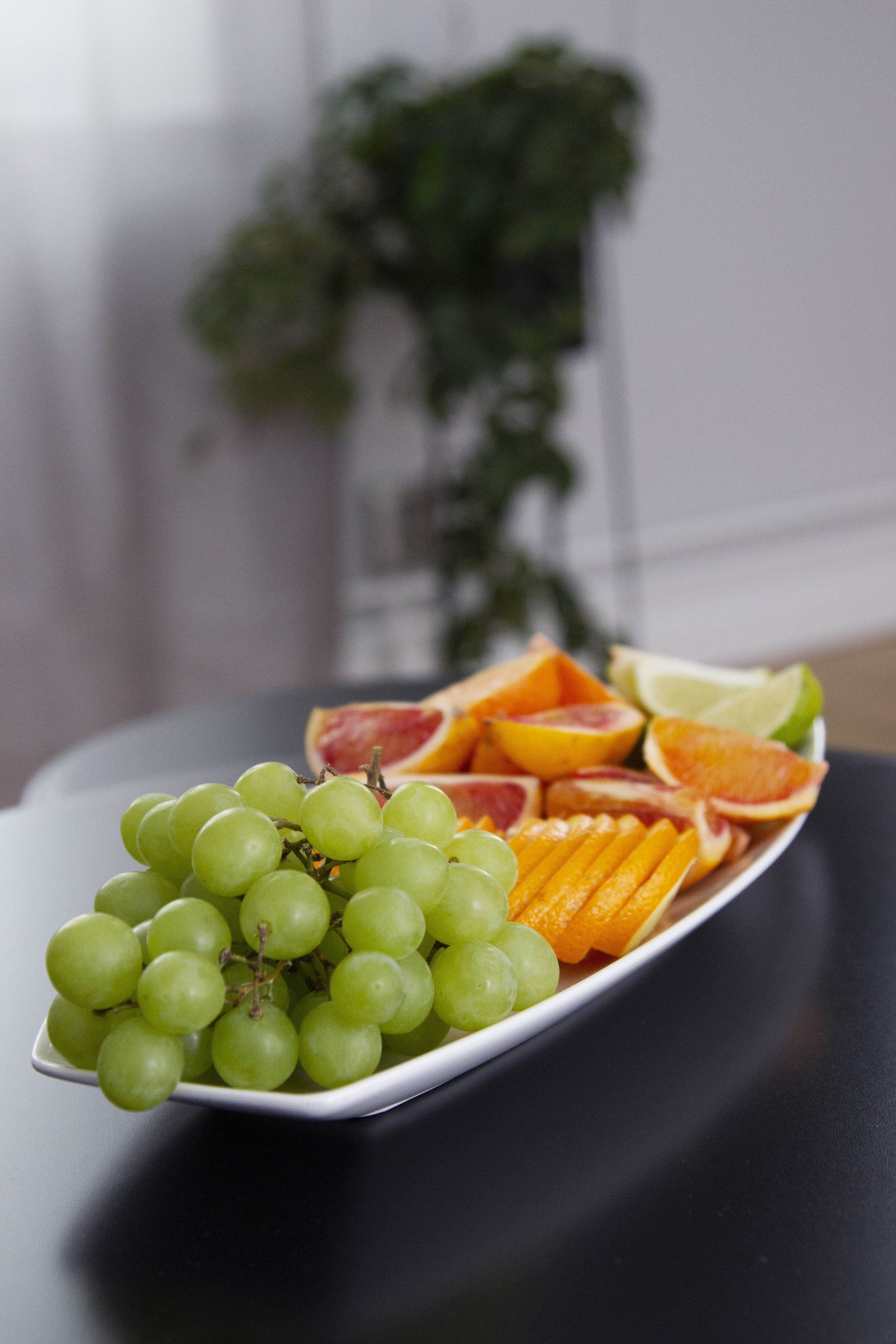 A plate of fruit including grapes, oranges, and blood oranges on a black table.