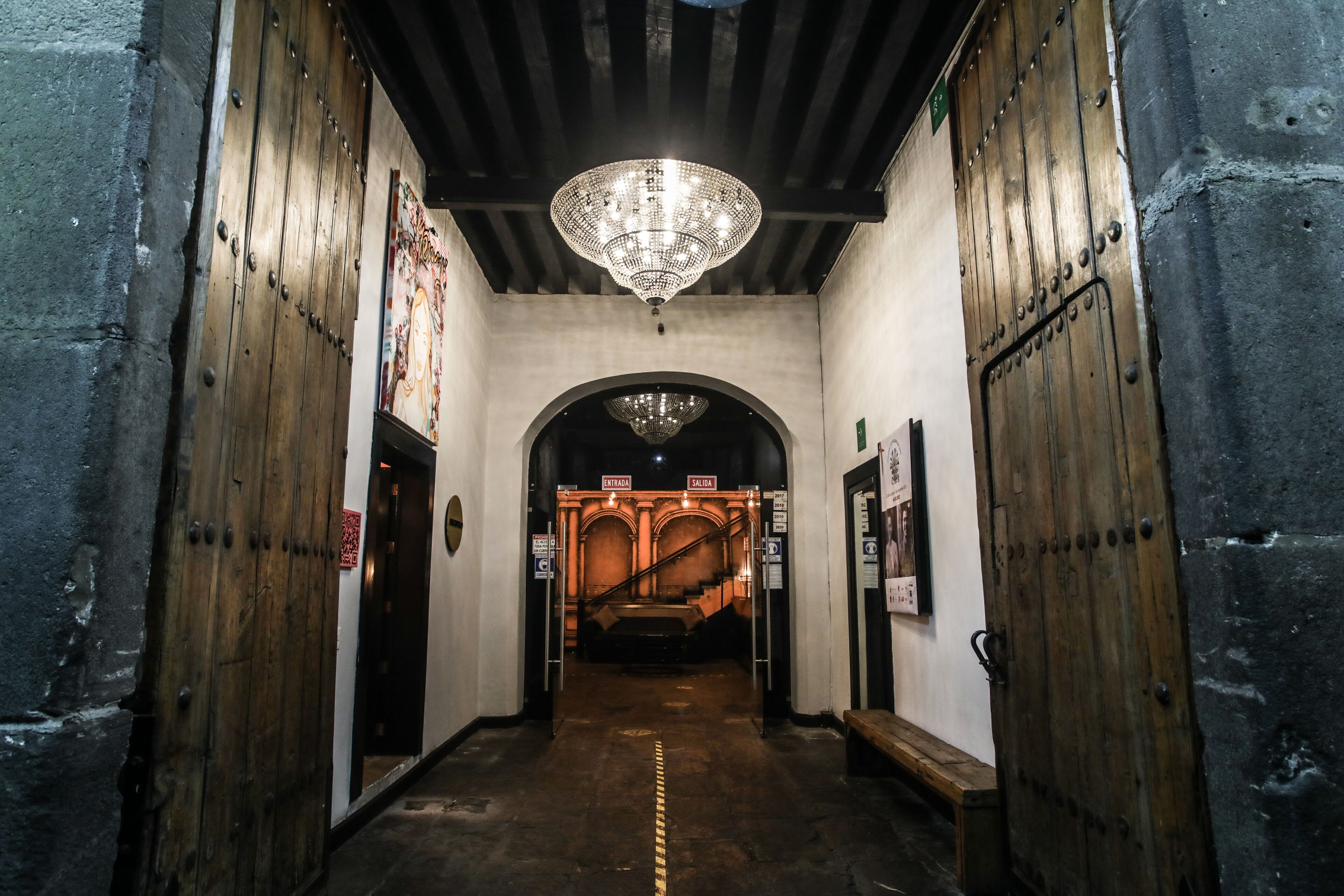 A corridor with wooden doors, a chandelier, and an arched passageway.