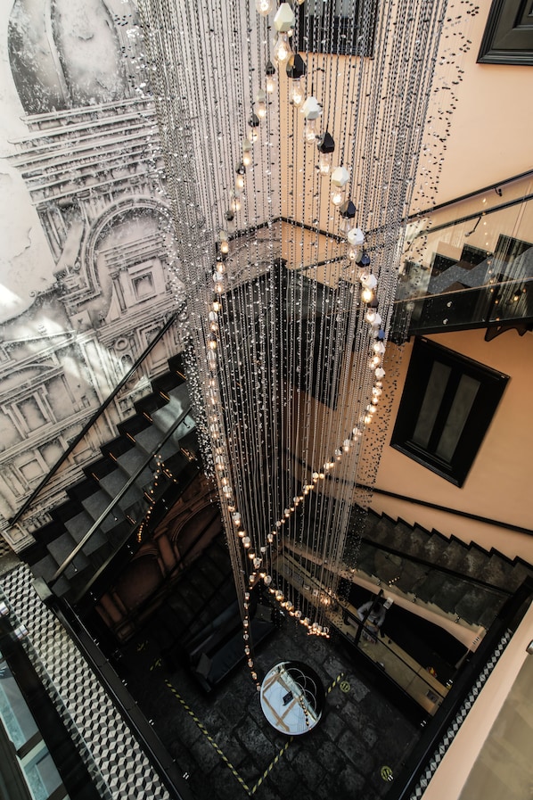 A high-ceiling atrium with a central spiral staircase, surrounded by hanging lights and a mural of architectural details.