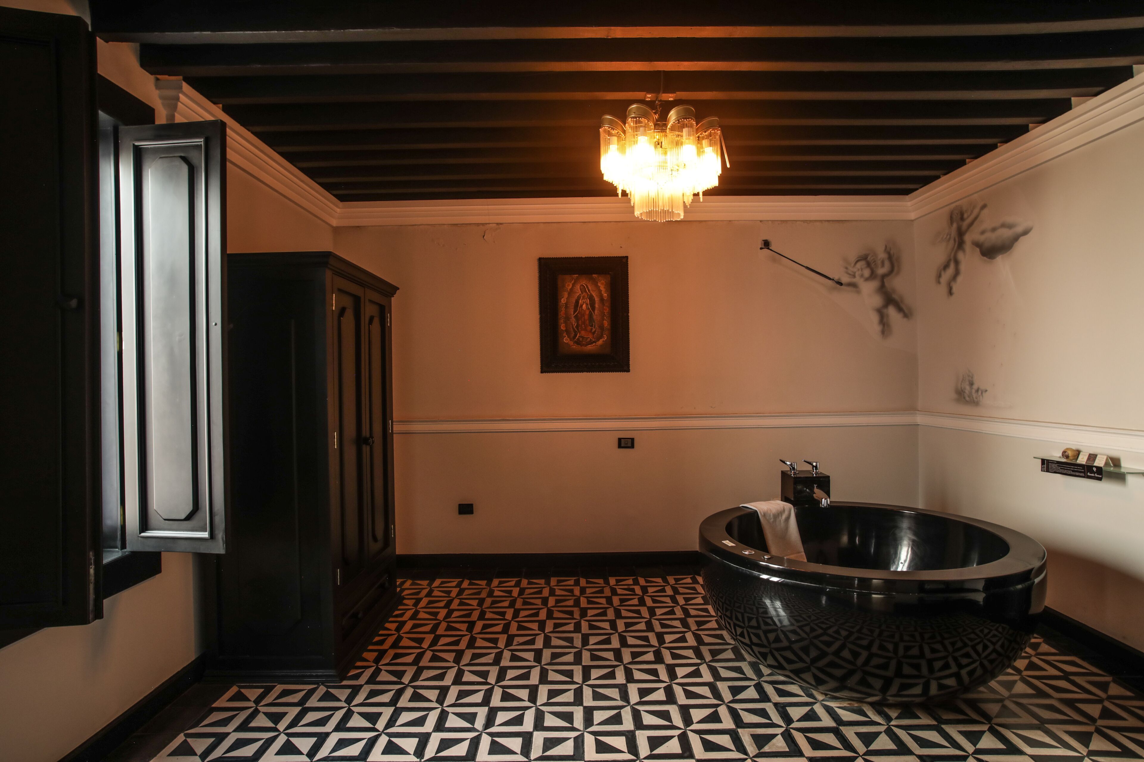 Een badkamer met een zwart bad, vloer met een geometrisch patroon, een kroonluchter en een kunstwerk in een lijst aan de muur.