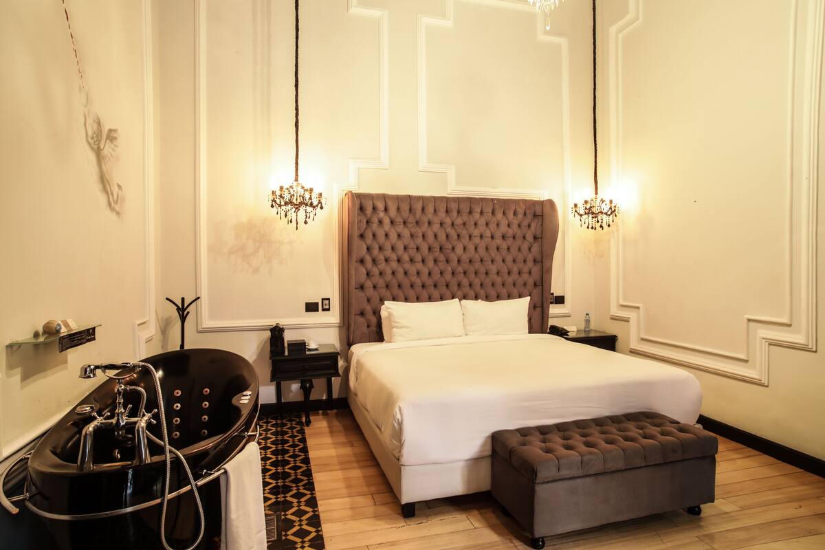A bedroom with a large bed, a bathtub, and two nightstands.