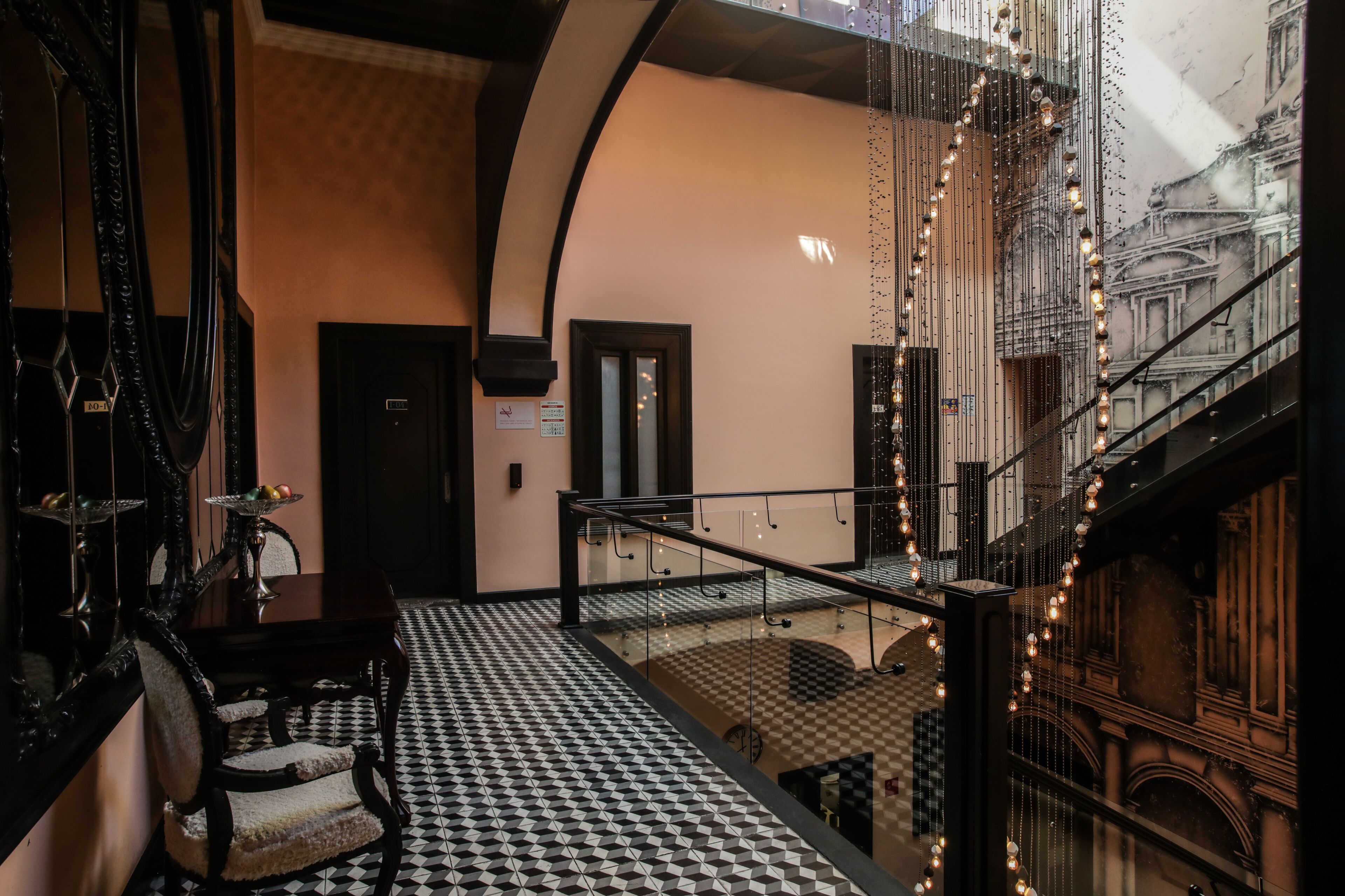 A hotel lobby with a checkered floor, a staircase, and a view of the cityscape through large windows.