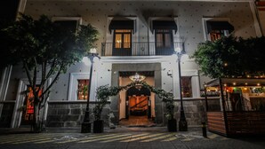 Un edificio histórico con una entrada imponente, una escalera que conduce al piso superior y un pequeño espacio al aire libre con guirnaldas de luces.