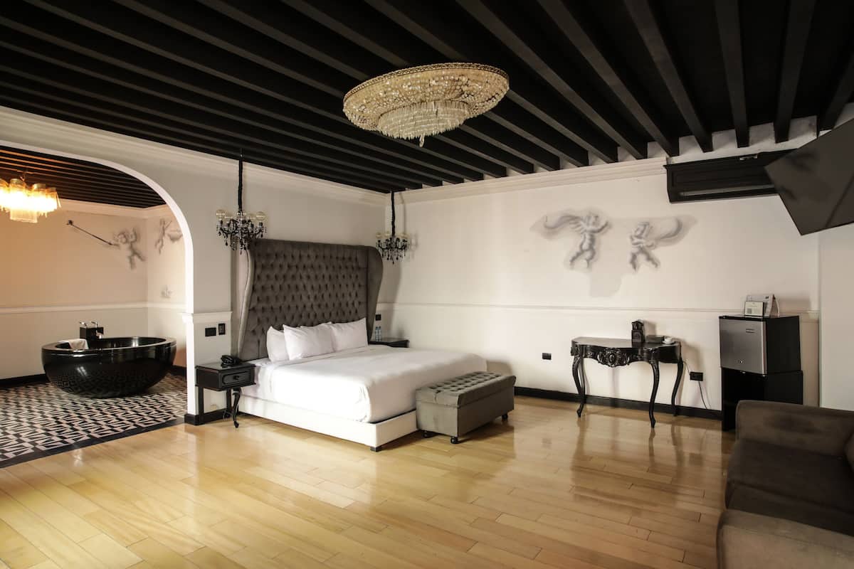 A modern bedroom with a large bed, a black bathtub, and a chandelier.
