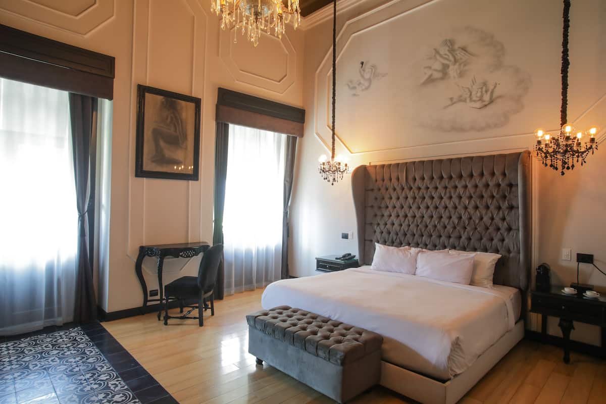 A large bed with a tufted headboard, a bedside table, a chair, and a chandelier.