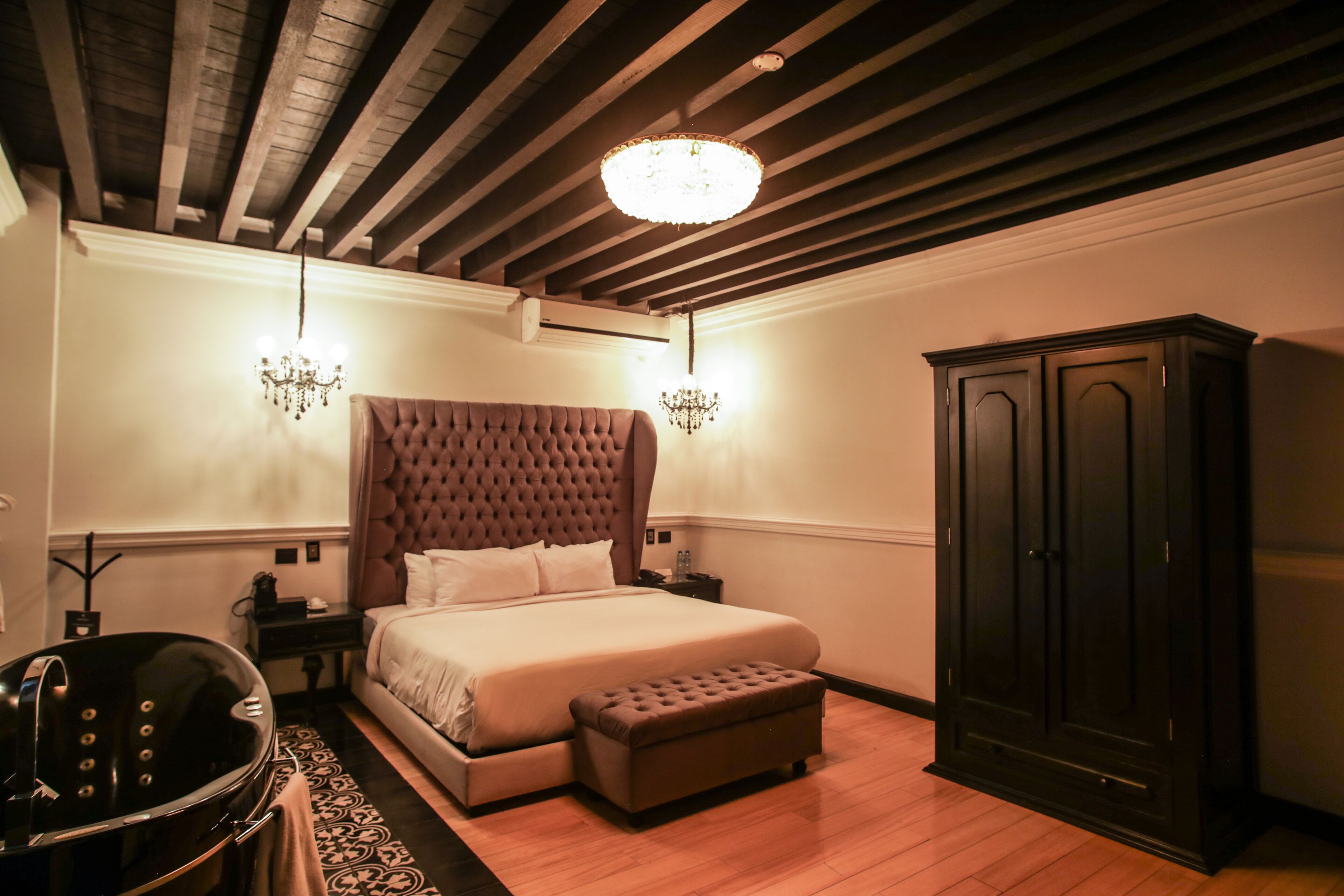 A bedroom with a large bed, a chest of drawers, a bench, and a bathtub.
