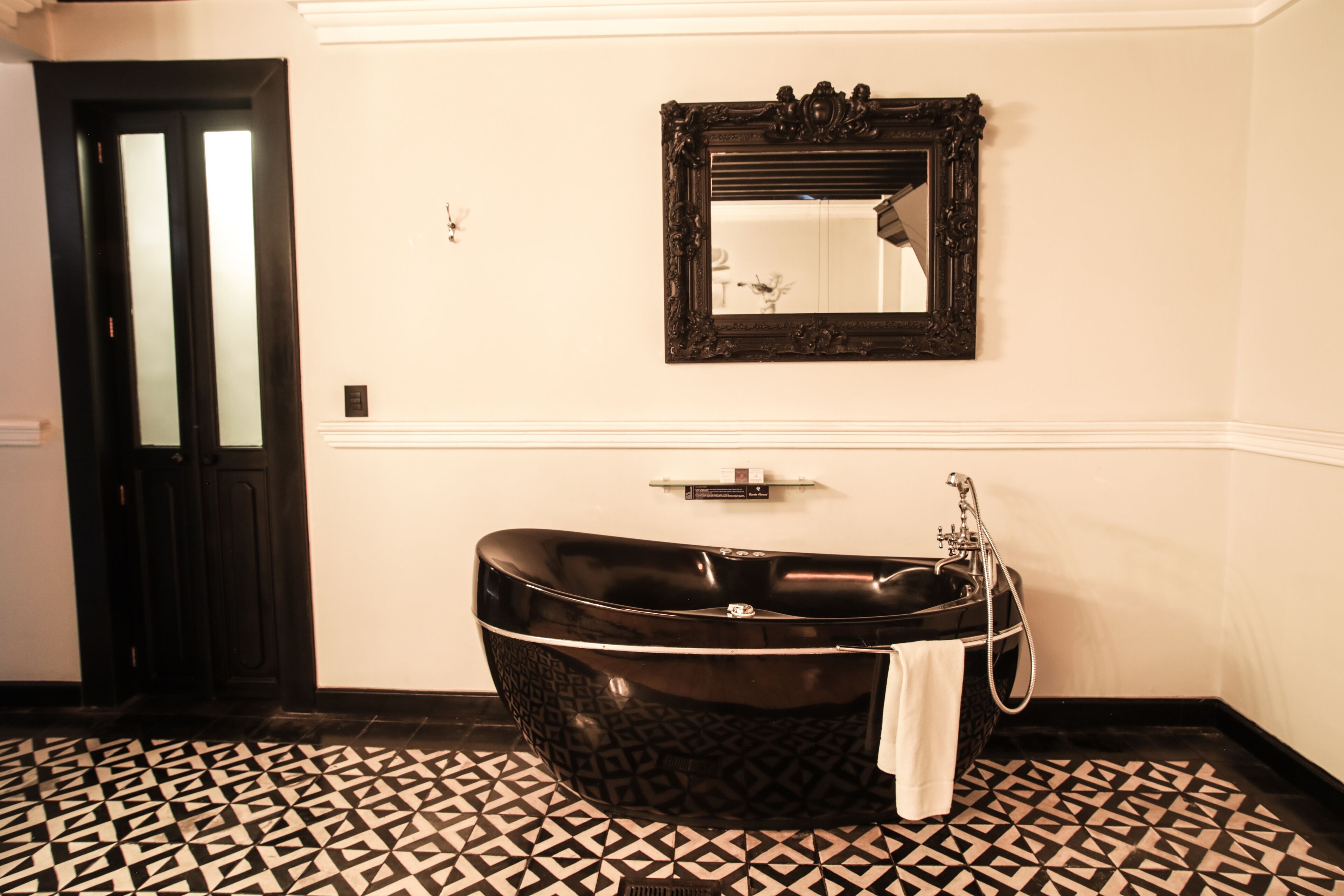 A bathroom with a freestanding bathtub, a mirror above it, and a patterned floor.