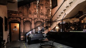 Un vestíbulo de hotel con una escalera monumental, un piano y una zona de estar con una mesa redonda.