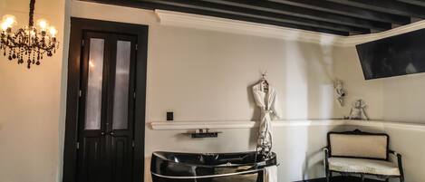 A hotel room with a black bathtub, a bench, a chandelier, and a wall-mounted TV.