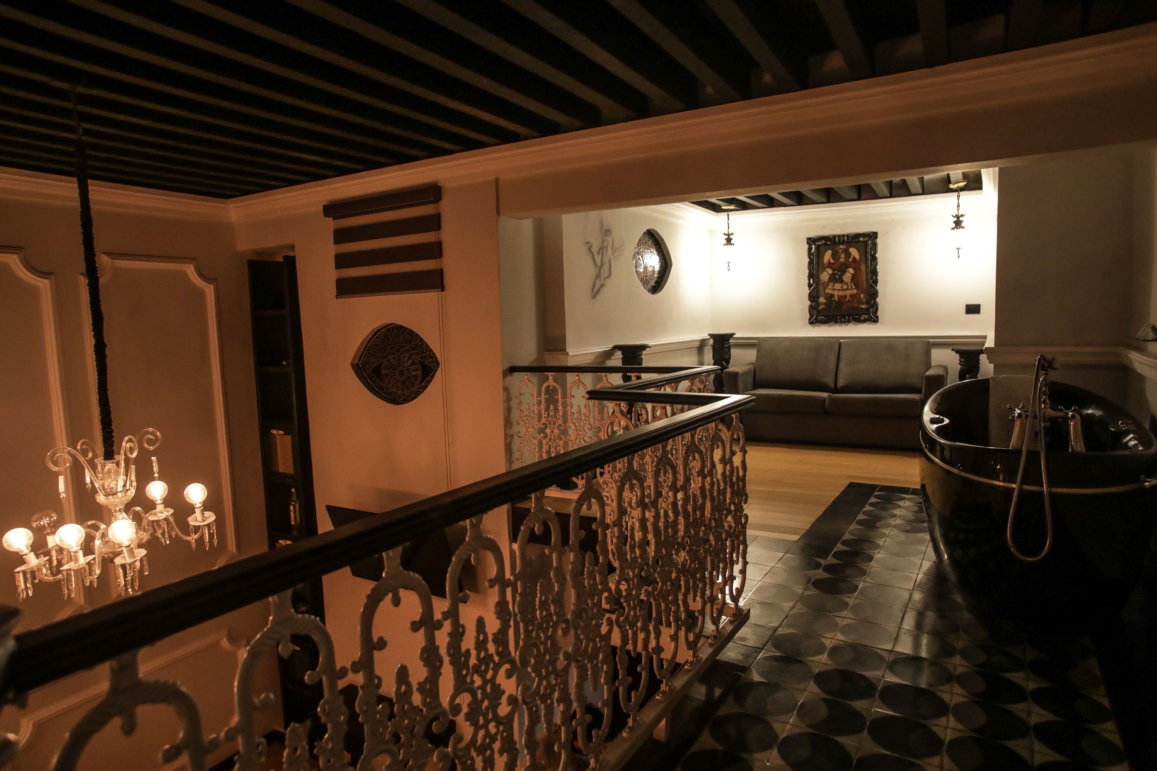 A dimly lit interior with a staircase, a chandelier, a sofa, and a painting on the wall.