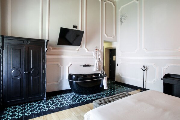 Een moderne hotelkamer met een groot bed, een zwart bad en een televisie die aan de muur is bevestigd.