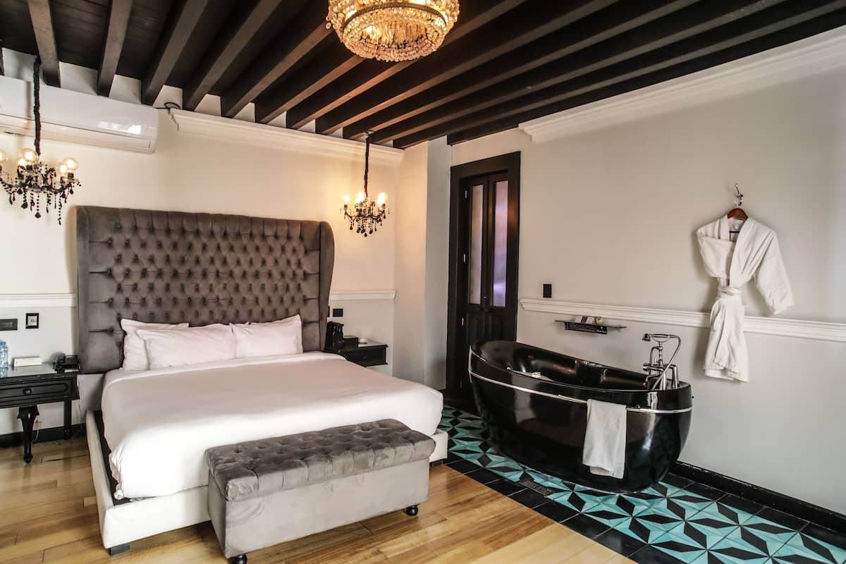 A bedroom with a large bed, a black bathtub, and a robe hanging on the wall.
