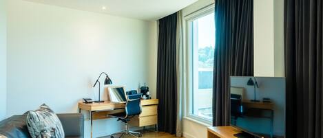 Una sala moderna con un escritorio de madera, un sofá cómodo, un televisor y un amplio ventanal con cortinas.