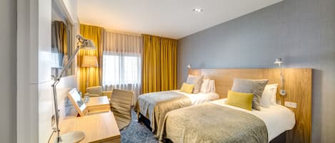 A hotel room with two beds, a desk, a chair, and a lamp.