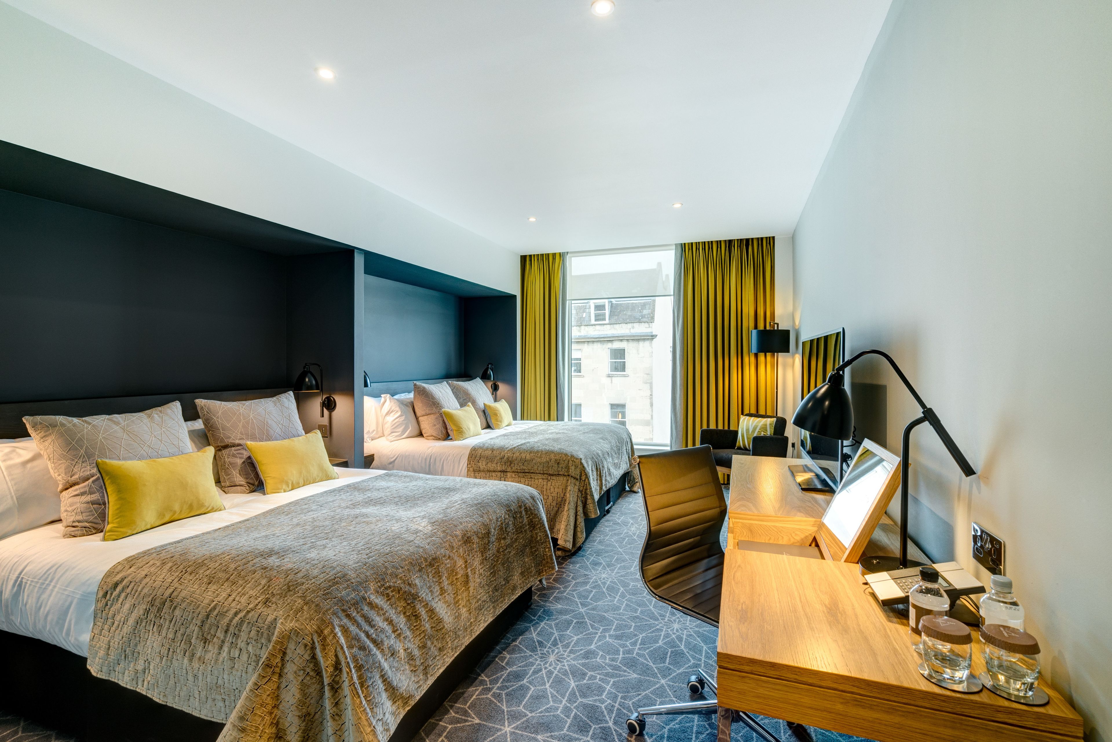 A modern hotel room with two beds, a desk, and a view of the city.