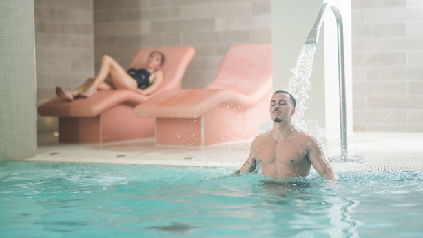 A man in a swimming pool with a water jet, and a woman relaxing on a lounge chair in the background. - Apex City of Bath Hotel (Bath)