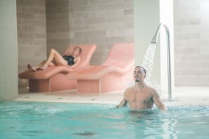 A man in a swimming pool with a water jet, and a woman relaxing on a lounge chair in the background. - Apex City of Bath Hotel (Bath)