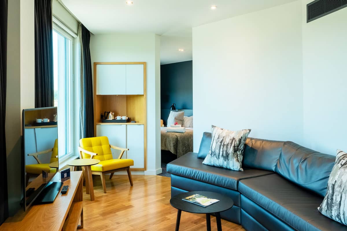 Ein modernes Wohnzimmer mit einer Couch, einem gelben Sessel, einem kleinen Tisch und einem Schreibtisch mit Computer.