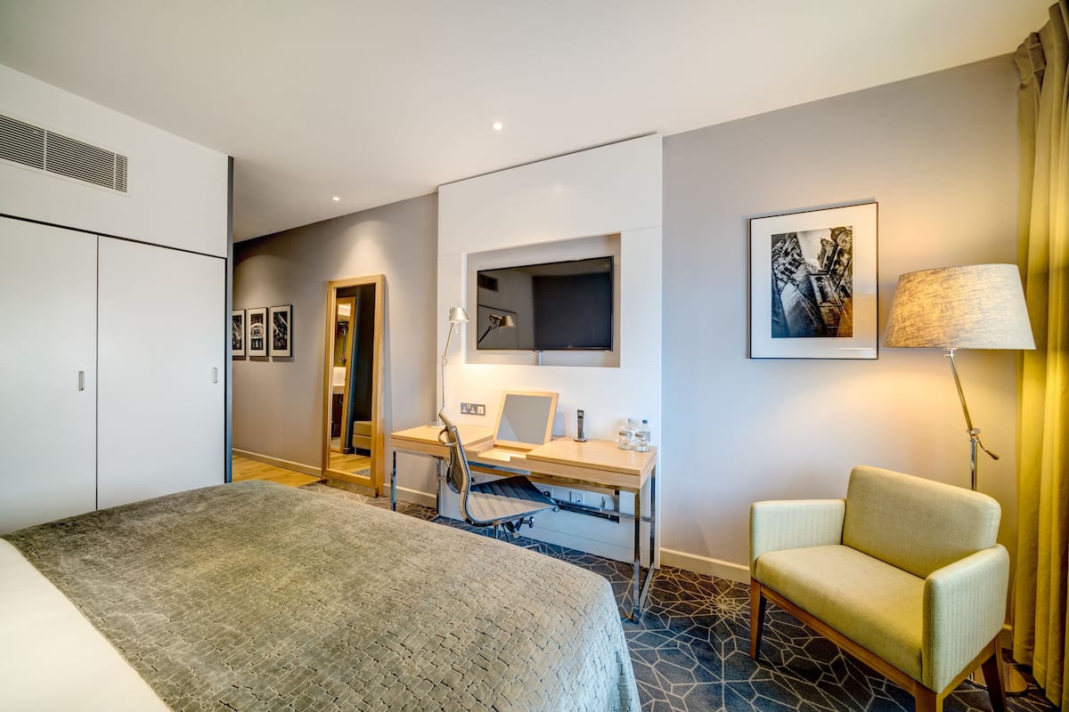Ein Hotelzimmer mit Bett, Schreibtisch mit Stuhl, Lampe und einem Bild an der Wand.