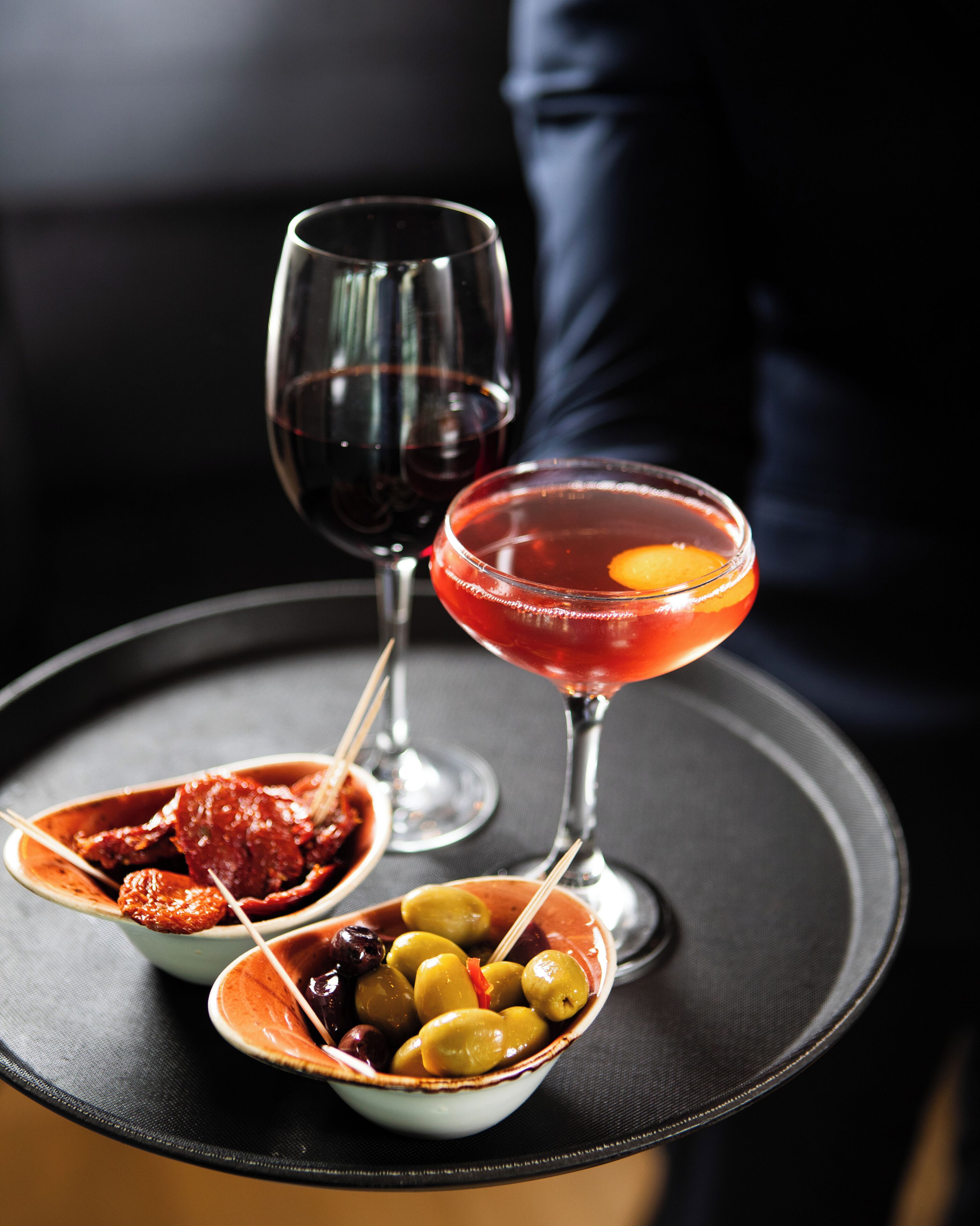 A table with a martini glass, a bowl of olives, and a dish of olives and cured meats.