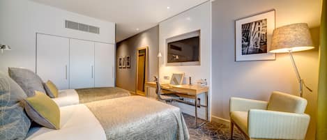 A hotel room with a bed, a desk, a chair, and a lamp.