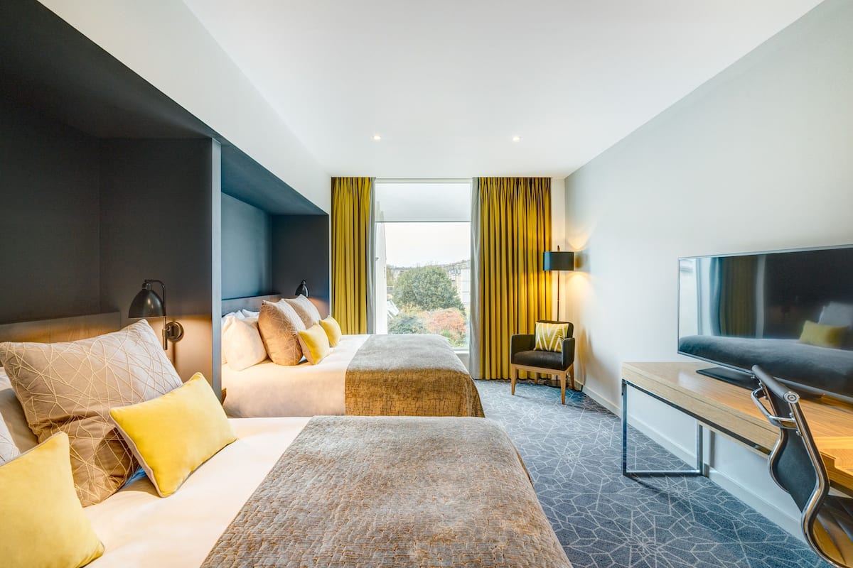 Ein modernes Hotelzimmer mit einem großen Bett, einem Schreibtisch mit Fernseher und Blick ins Freie.