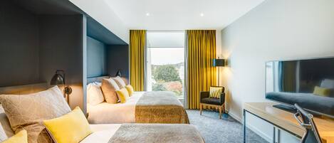 A modern hotel room with a large bed, a desk with a TV, and a view of the outdoors.