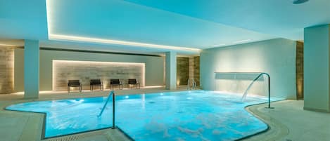 Una piscina interna dal design moderno, con un pavimento a mosaico blu particolare e una zona relax con sedute.