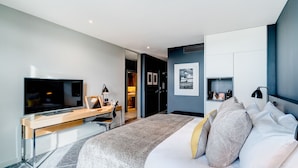 A modern hotel room with a large bed, a desk with a flat-screen TV, a wardrobe, and a small seating area. - Apex City of Bath Hotel (Bath)