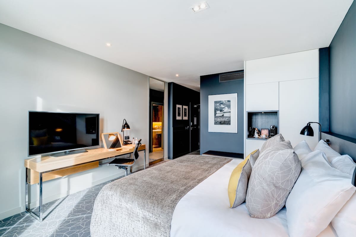 Ein modernes Hotelzimmer mit einem großen Bett, einem Schreibtisch mit Flachbildfernseher, einem Kleiderschrank und einer kleinen Sitzecke.