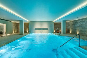 An indoor swimming pool with a clear view of the water, a bench on the left, and a wall with a textured pattern. - Apex City of Bath Hotel (Bath)