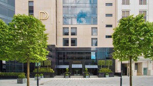A modern building with a prominent 'D' logo, featuring a glass facade and a well-maintained courtyard with trees. - Dakota Leeds (Leeds)